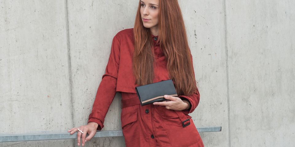 Žena s ryšavými vlasmi v oranžovom kabátiku drží koženú peňaženku Caleo Woman Wallet